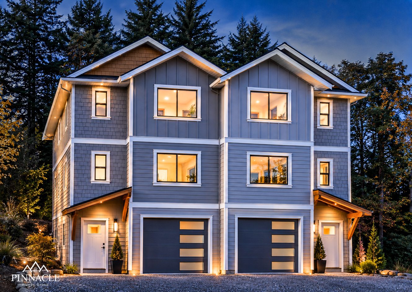 Coastwoods Phase 1 townhomes at dusk, grey board and batten siding with shingle gables and garages