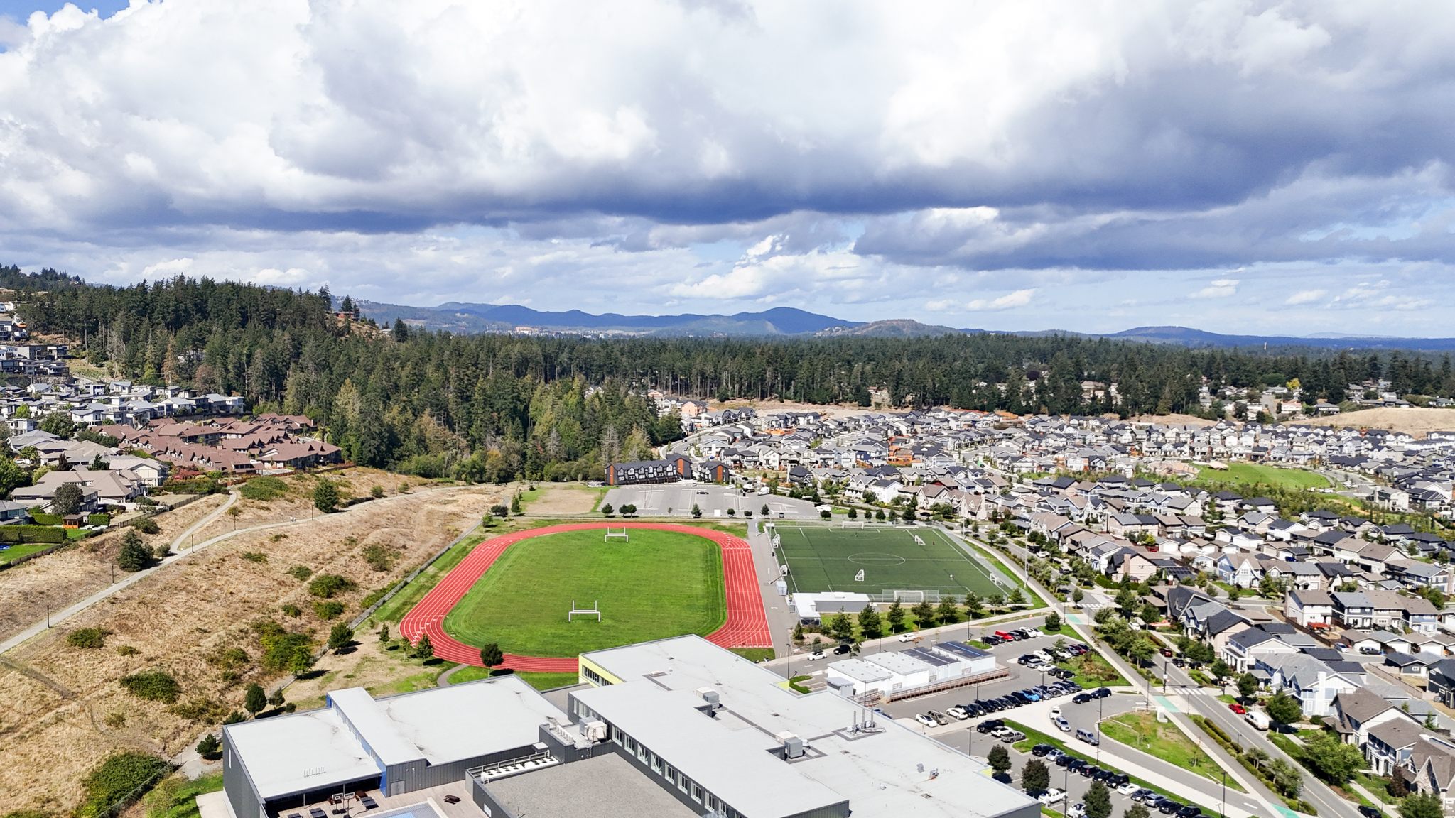 Aerial view of West Shore sports fields and a running track in Colwood with wooded hills behind
