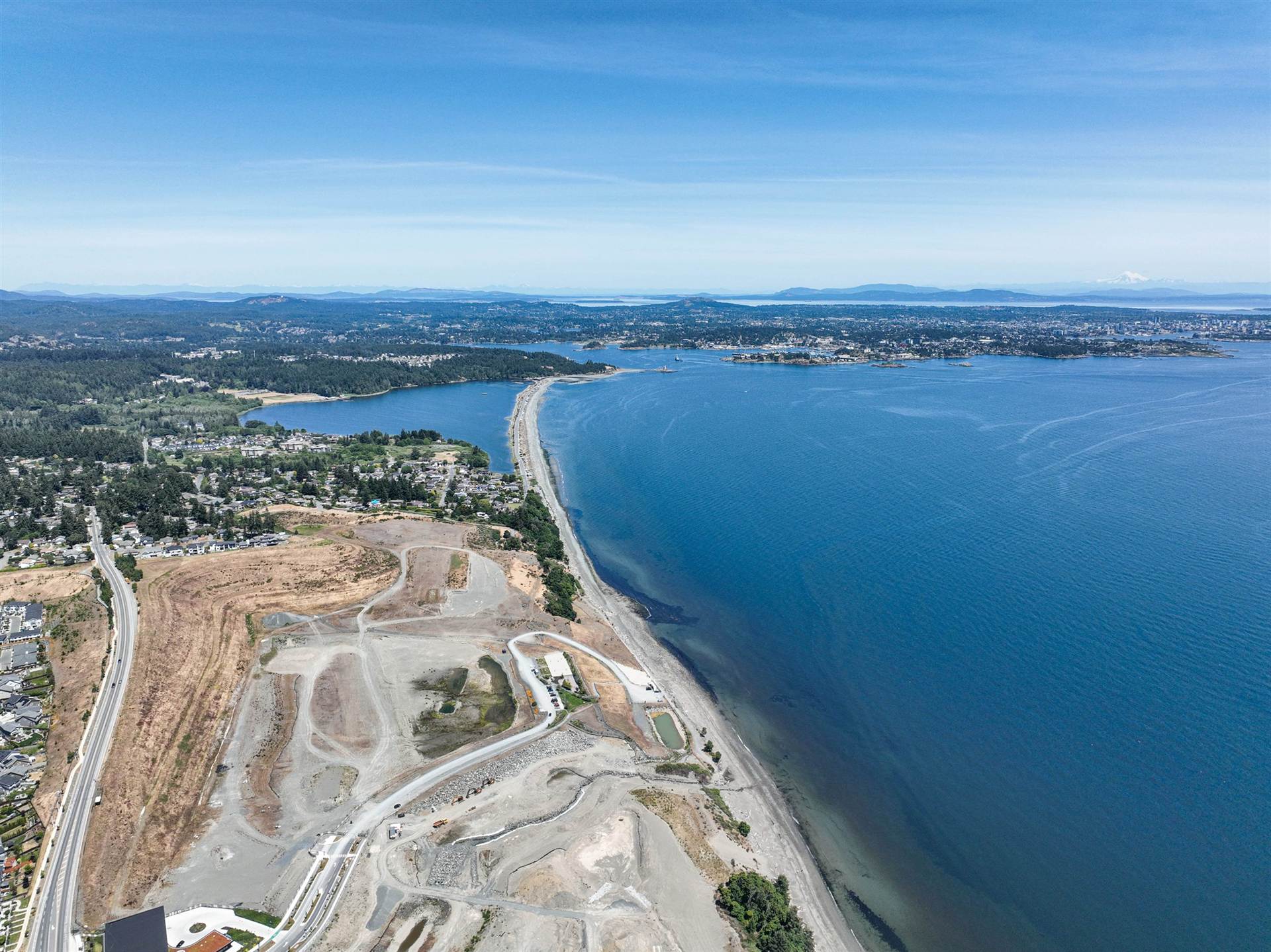 Aerial view of the Salish Sea shoreline at Royal Bay in Colwood, with the beach spit, the Victoria skyline and mountains on the horizon