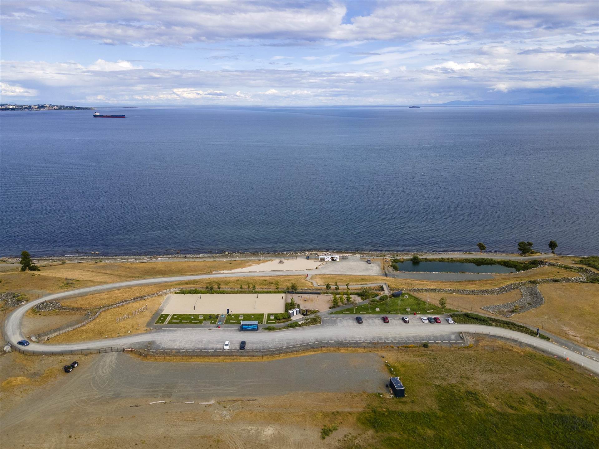 Aerial view of the beach park at Royal Bay in Colwood, with sand volleyball courts and freighters anchored offshore