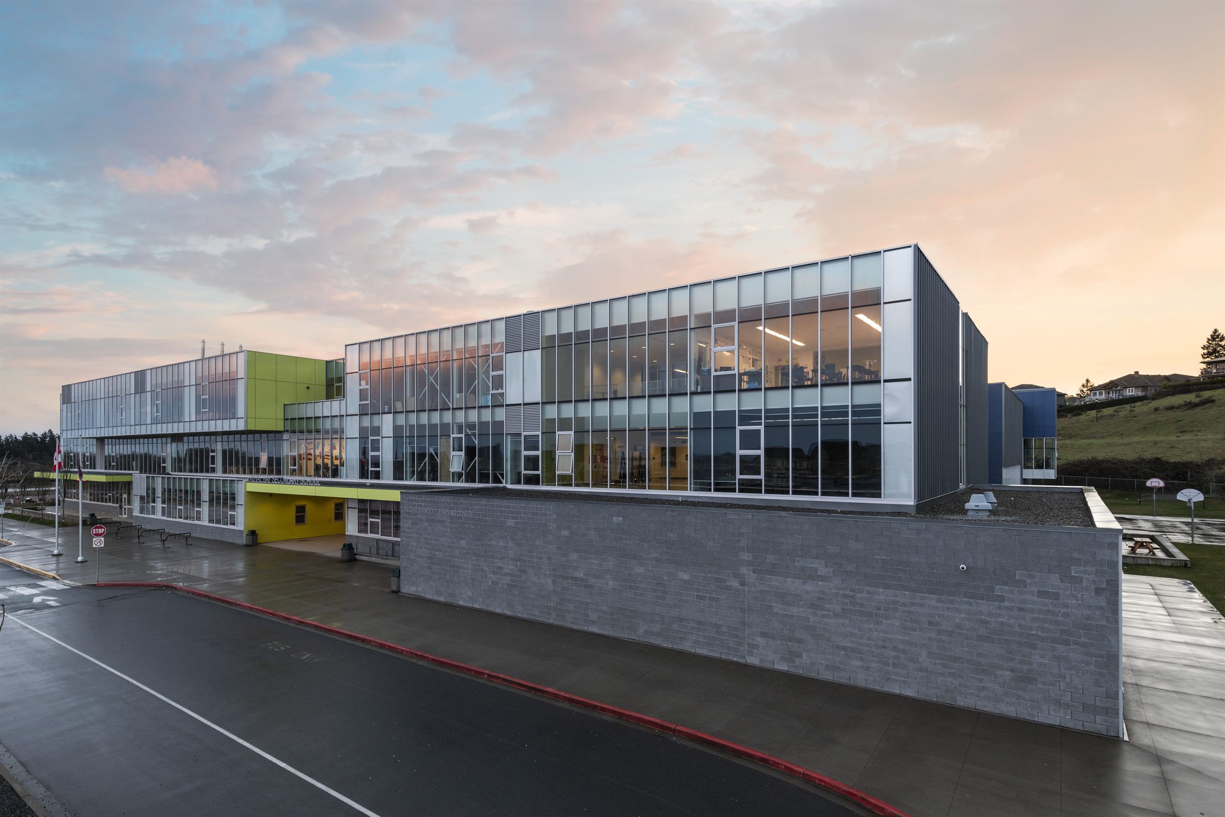Exterior of Royal Bay Secondary School in Colwood at dusk, glass and metal facade under a pink sky